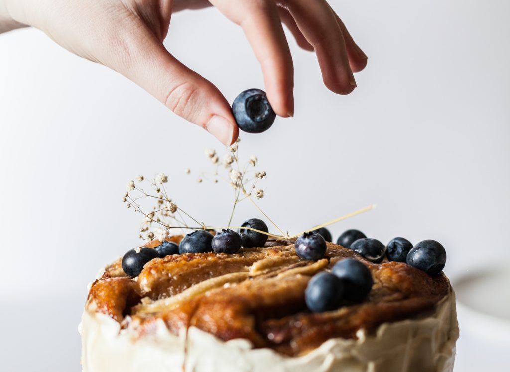hand placing a blueberry on cake baking