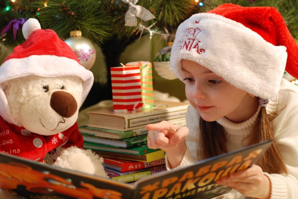 little girl with santa hat reading with her toy teddy