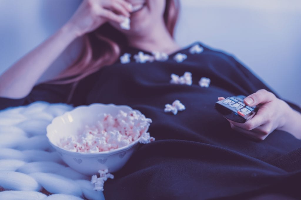 lady in black top eating popcorn and holding remote