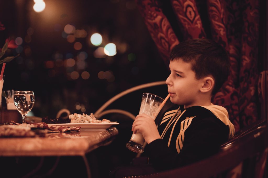 boy drinking milkshake from glass in front of table