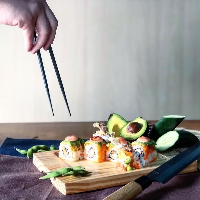 Hand holding chopsticks over plate of sushi