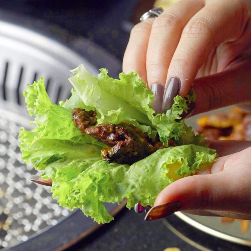 woman with nail painted nails wrapping grilled meat in lettuce