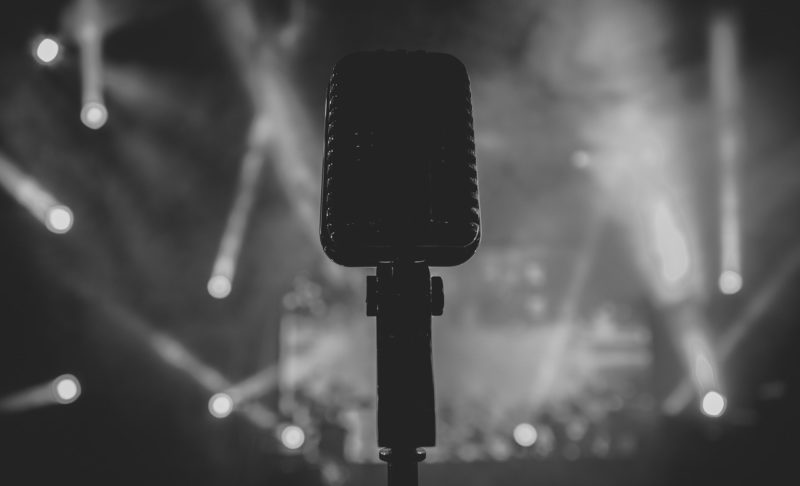 Black and white photo of a microphone with audience in the background