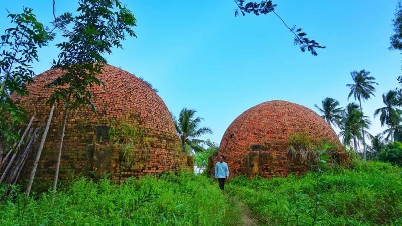 man walking between brick red igloo amongst green plantation