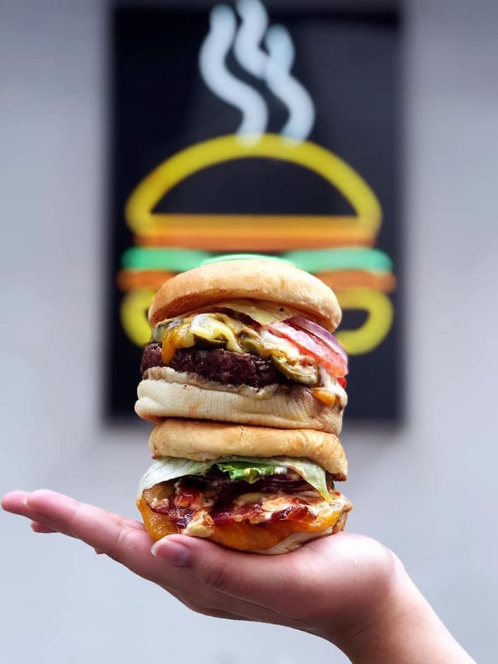 two burgers stacked on top of a female hand