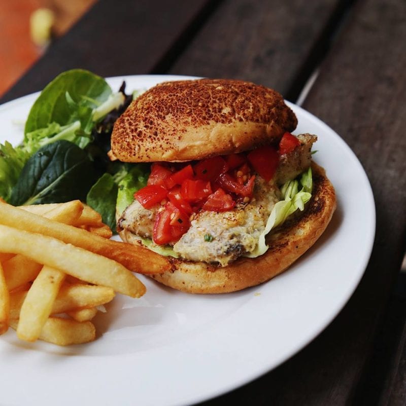 cod fish burger with homemade sauce topped with cherry tomatoes and served with fries and salad